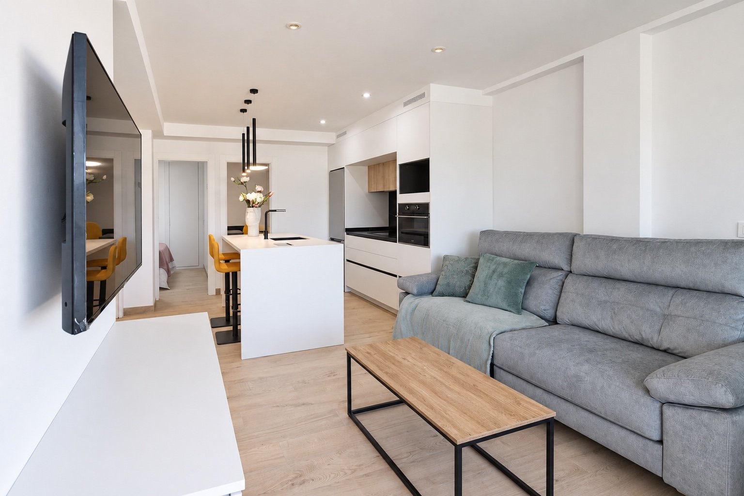 Salón con sofá gris, cocina blanca e isla central en una reforma integral de apartamento