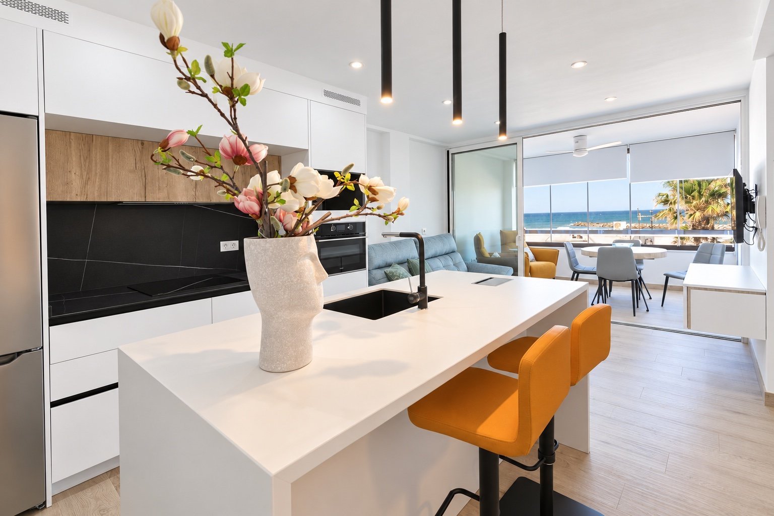 Cocina blanca con isla, taburetes mostaza y vistas al mar desde la terraza en Almerimar