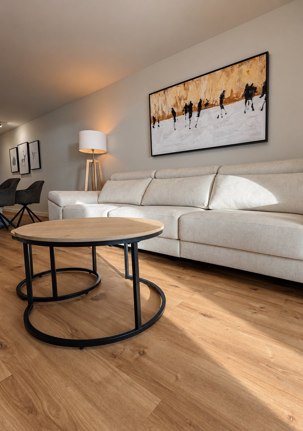 Salón con suelo de madera, mesas auxiliares y sofá claro atravesado por luz natural