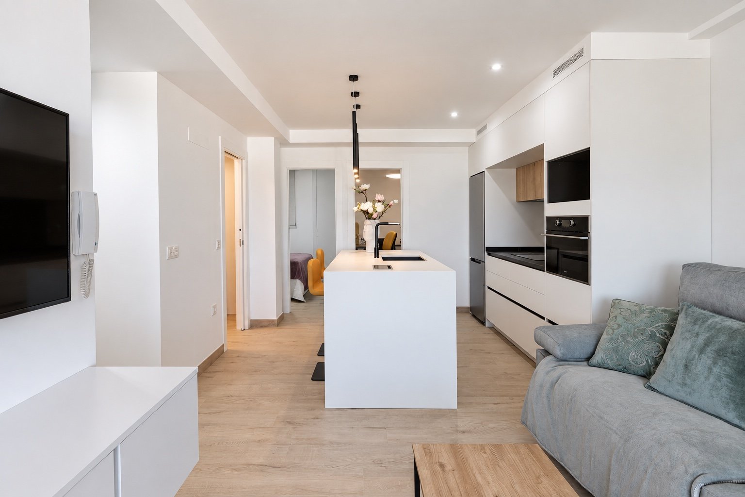Vista axial del pequeño apartamento con isla central, cocina lineal y circulación hacia el dormitorio