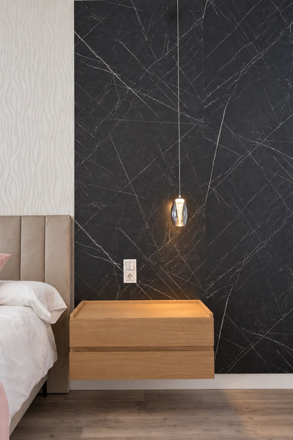 Detalle de pared de piedra negra veteada junto a cabecero tapizado y mesita de madera