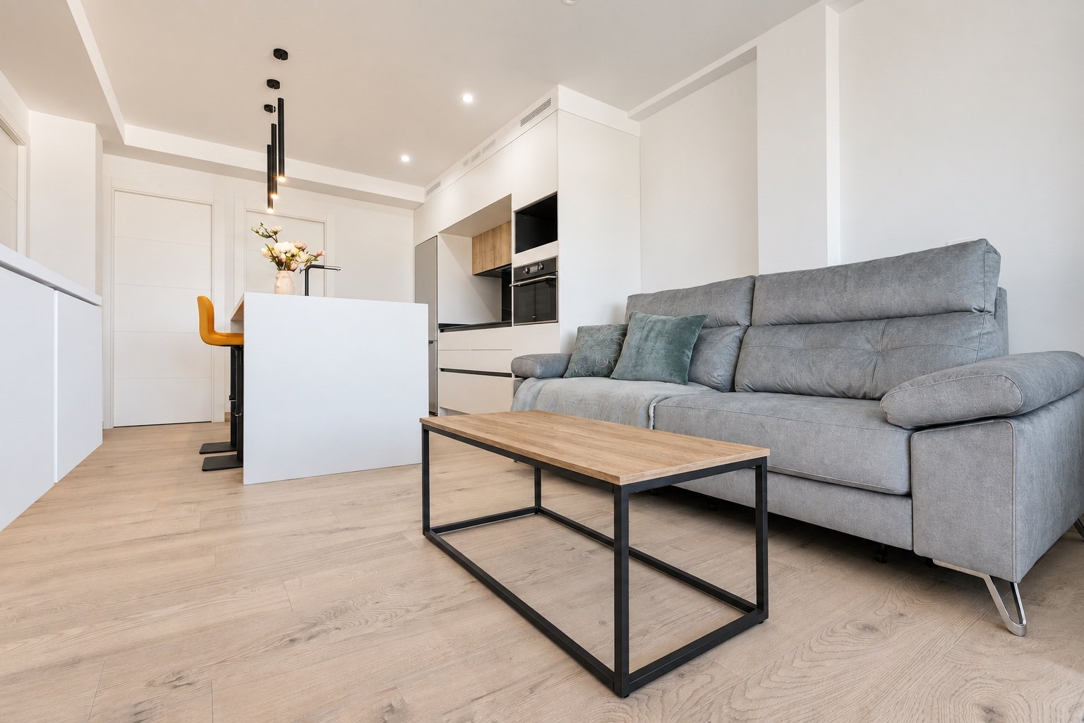 Vista baja del salón con sofá gris y mesa de madera conectado con la cocina abierta