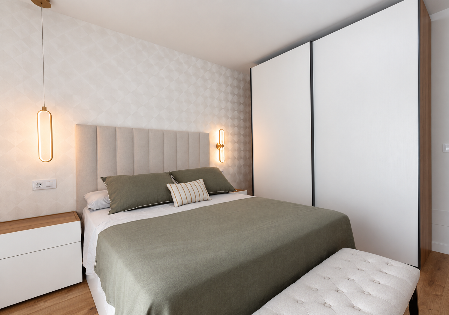 Vista diagonal del dormitorio con armario blanco, banco tapizado y luces cálidas